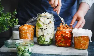 Kimchi selber machen im Glas: Verschiedene fermentierte Gemüse in Gläsern, darunter ein Glas mit rotem Kimchi, das gerade mit einer Gabel entnommen wird.
