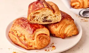Zwei goldbraune, knusprige Pain au Chocolat auf einem Teller, eines davon angeschnitten, enthüllt die schokoladige Füllung.