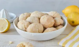 Schüssel voller zitronen cookies, daneben Zitronen und ein Zitronenpresse. Ein Cookie ist angebrochen.