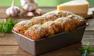 Herzhaftes Monkey Bread mit Knoblauch und Käse, frisch aus der Form. Daneben liegen Knoblauchzehen und Petersilie.