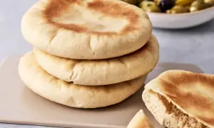 Gestapeltes pita brot mit einer Schüssel Oliven im Hintergrund. Ein Stück ist aufgeschnitten und zeigt die weiche Krume.