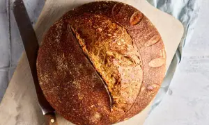 Ein rustikales Dinkel Sauerteigbrot mit knuspriger Kruste und luftiger Krume liegt auf einem Holzbrett neben einem Messer.