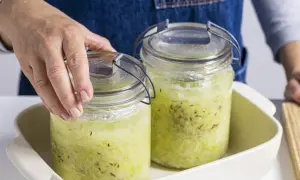 Hände setzen zwei Gläser mit Sauerkraut zum Fermentieren in ein Gefäß.