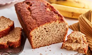 Ein saftiges, goldbraunes bananenbrot glutenfrei, mit zwei Scheiben auf einem Silbertablett und reifen Bananen im Hintergrund.