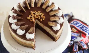 Eine köstliche Snickers Torte mit Schokoladenglasur, Erdnüssen und Sahnetuffs. Kleine Snickers-Stücke zieren den Rand.