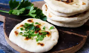 Frisch gebackenes naan brot, bestreut mit Petersilie, liegt auf einem Holzbrett neben einem Stapel weiterer Fladenbrote.