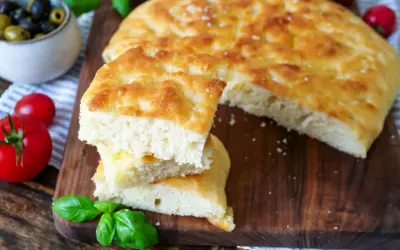 Frisch gebackenes Focaccia-Rezept, aufgeschnitten und gestapelt, mit Tomaten und Oliven daneben.