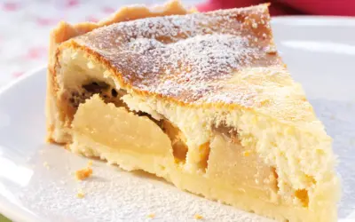 Ein Stück Apfelkuchen mit Quark, bestäubt mit Puderzucker, auf einem weißen Teller.