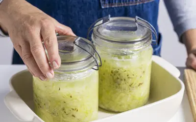 Hände setzen zwei Gläser mit Sauerkraut zum Fermentieren in ein Gefäß.