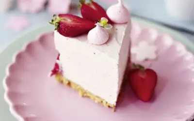 Ein Stück Erdbeer Cheesecake mit frischen Erdbeeren und Baiser-Tupfern auf einem rosa Teller.