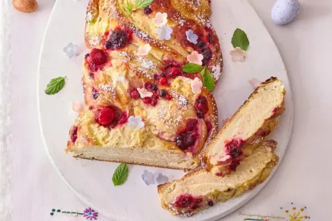 Ein köstlicher Osterzopf mit Quark und Beeren, bestäubt mit Puderzucker und verziert mit Minze und kleinen Blüten.