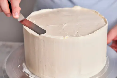 Eine Hand glättet mit einem Spatel die cremige Buttercreme-Torte.