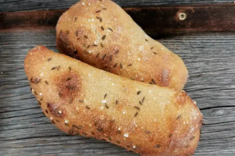 Zwei frisch gebackene Seelen mit Kümmel und Salz auf rustikalem Holz.