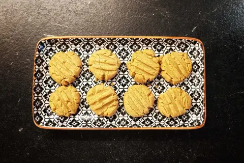 A rectangular plate with a black and white floral pattern holds eight golden-brown kekse ohne zucker.