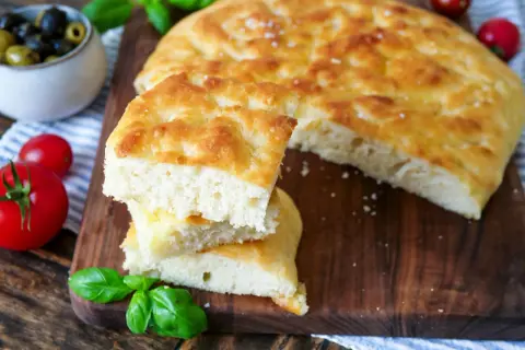 Frisch gebackenes Focaccia-Rezept, aufgeschnitten und gestapelt, mit Tomaten und Oliven daneben.