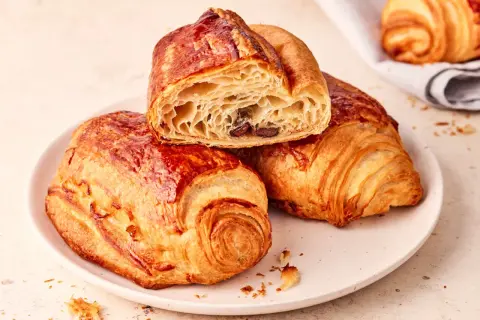 Zwei goldbraune, knusprige Pain au Chocolat auf einem Teller, eines davon angeschnitten, enthüllt die schokoladige Füllung.