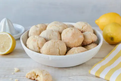 Schüssel voller zitronen cookies, daneben Zitronen und ein Zitronenpresse. Ein Cookie ist angebrochen.