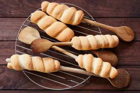Frisch gebackenes Stockbrot mit frischer Hefe, auf Holzkochlöffeln auf einem Gitterrost arrangiert.