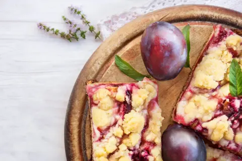 Saftiger Zwetschgenkuchen vom Blech mit Streuseln, garniert mit frischen Pflaumen und Minze.