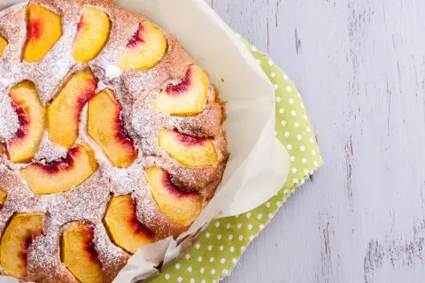 Saftiger Pfirsichkuchen, mit Puderzucker bestäubt, auf einem grünen Tupftuch. Ein Genuss für die Sinne!