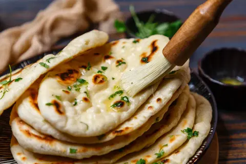 Frisch gebackenes indisches Fladenbrot wird mit Butter bestrichen und mit Koriander bestreut.