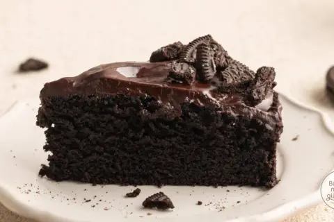 Ein Stück saftiger Oreo Kuchen mit glänzender Schokoladenglasur und zerbröselten Keksen obendrauf.