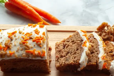 Saftiger karottenkuchen mit cremigem frosting, garniert mit geriebenen Karotten und Walnüssen. Daneben liegen frische Karotten und Nüsse.