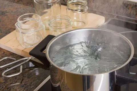 Gläser werden für das Einkochen mit Schraubdeckel sterilisiert. Ein Topf mit kochendem Wasser und ein Glasheber liegen bereit.