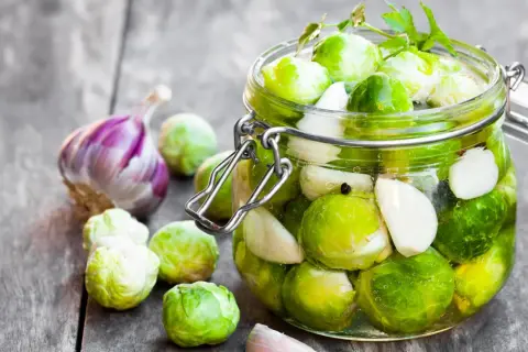 Frischer Rosenkohl und Knoblauch werden für das Rosenkohl einlegen in ein Glas gefüllt.