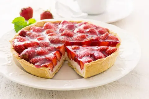 Ein saftiger Erdbeerkuchen mit Quarkfüllung, bedeckt mit frischen Erdbeeren und glänzendem Tortenguss. Ein Stück ist bereits entnommen.