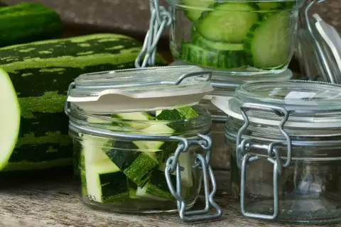 Zucchini-Scheiben und -Würfel in Gläsern, bereit zum einkochen im Dampfgarer. Frische Zucchini liegt daneben.