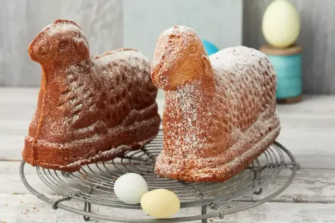 Zwei goldbraune Osterlämmer, mit Puderzucker bestäubt, auf einem Gitter. Ein perfektes Osterlamm Rezept für das Fest.