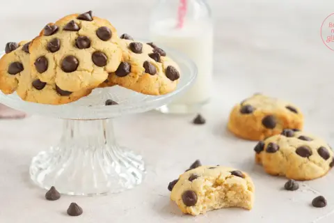 Saftige low carb Kekse mit Schokostückchen auf einem Glasständer, daneben ein Glas Milch und weitere Kekse.