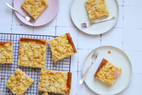 Saftiger Rhabarberkuchen auf Hefeteig mit Streuseln, auf Tellern und einem Kuchengitter arrangiert.