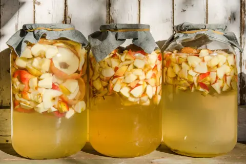 Drei Gläser mit Apfelschnitzen und Flüssigkeit, bereit, um Apfelessig selber zu machen.