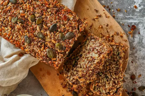 Brot ohne Mehl, reich an Saaten wie Kürbis- und Leinsamen, liegt auf einem Holzbrett.