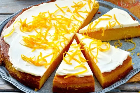 Ein saftiger, gesunder Kuchen mit weißem Zuckerguss und orangen Zesten verziert, auf einem silbernen Blech.