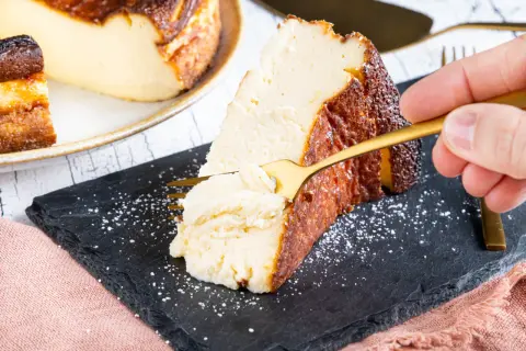 Ein Stück cremiger San Sebastian Cheesecake wird mit einer goldenen Gabel probiert.