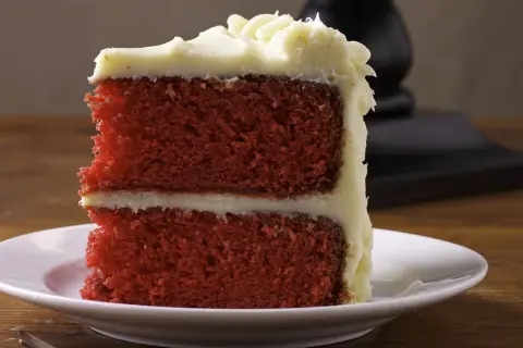 Ein Stück saftiger **red velvet** Kuchen mit cremiger Glasur auf einem weißen Teller.