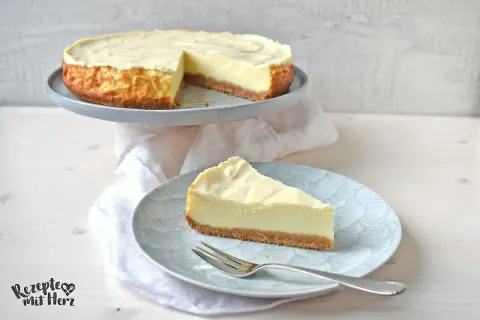 Ein cremiger american cheesecake mit Keksboden, ein Stück auf einem Teller mit Gabel.