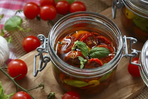 Eingeweckte Tomaten in Öl, garniert mit Basilikum. Die Haltbarkeit von Eingewecktem ist oft lang, wenn richtig gelagert.