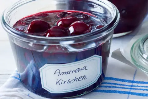 Ein Glas mit Amarena Kirschen, perfekt für ein Amarena Kirschen Rezept. Die dunklen Früchte schwimmen in Sirup.