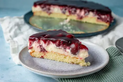 Ein saftiges Stück Kirsch Schmand Kuchen mit Kirschen und einer glänzenden Geleeschicht auf einem Teller.