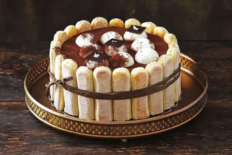 Eine köstliche Tiramisu Torte, umrandet von Löffelbiskuits und verziert mit Kakao und Schokoladenstückchen.