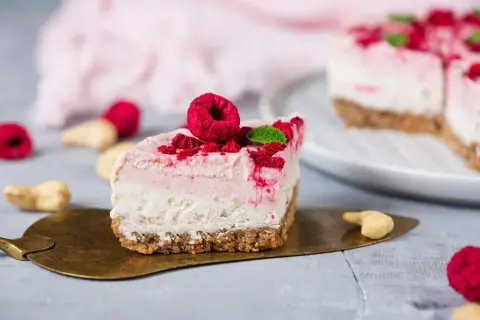 Ein Stück Himbeer Cheesecake mit frischen Himbeeren und Minze auf einem goldenen Tortenheber.