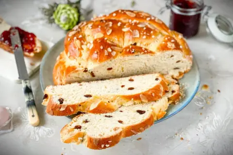 Ein goldbraunes Osterbrot mit Rosinen und Mandelsplittern, perfekt gebacken mit Trockenhefe. Dazu ein Glas Marmelade.