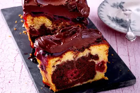 Saftiger Marmorkuchen mit Kirschen und Schokoladenglasur, auf einem dunklen Brett serviert.