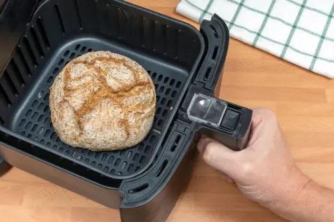Ein goldbraunes Brot liegt im Korb eines Airfryers. Perfekt für schnelles brot backen im airfryer.