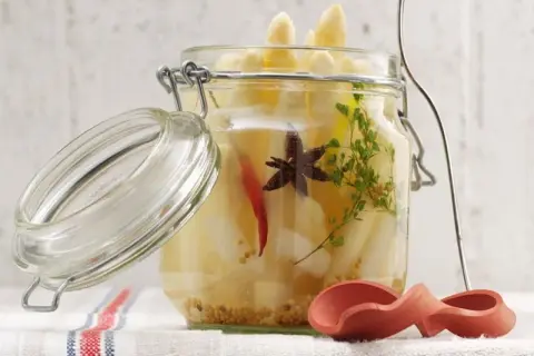 Ein Glas mit eingelegtem Spargel, Gewürzen und Kräutern. Der Deckel ist geöffnet.