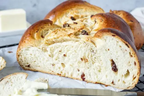 Ein goldbrauner Hefezopf mit Rosinen, frisch gebacken und bereit zum Genießen. Daneben liegt ein Stück Butter.